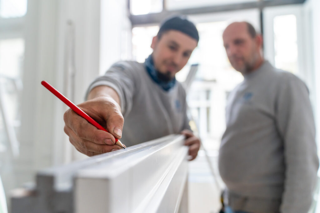 Deux techniciens Abihome examinant un profilé de dormant de porte blanc lors d'une installation.