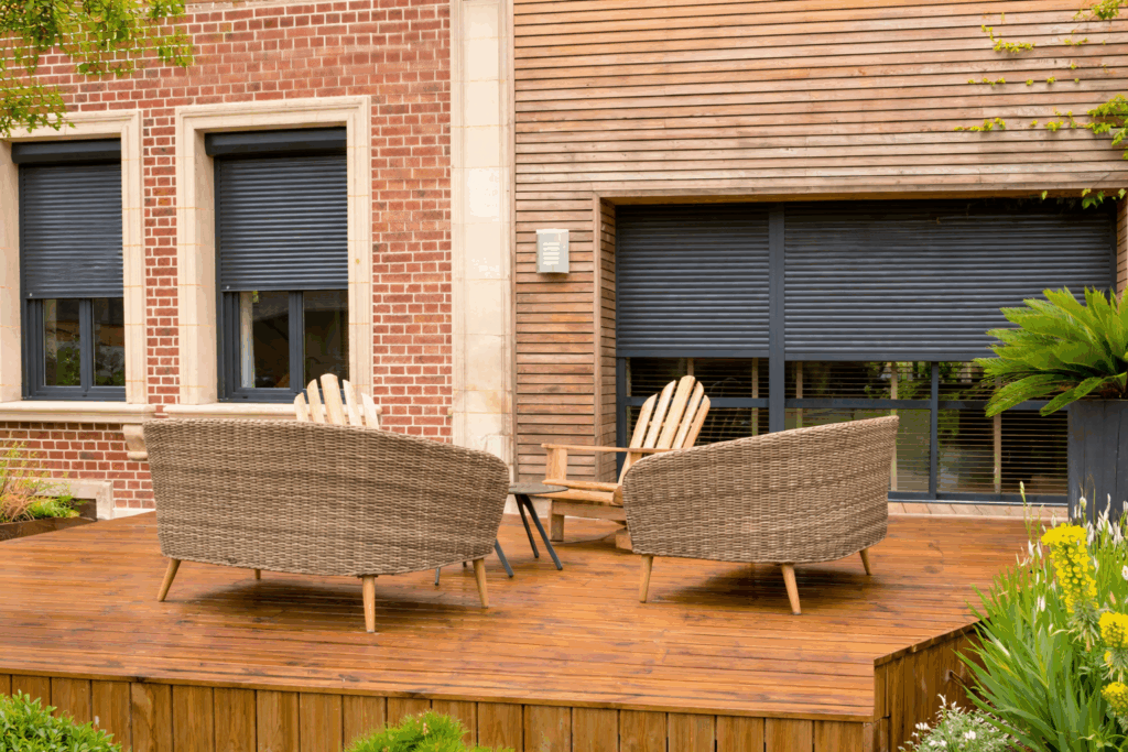 Terrasse en bois avec fauteuils en résine tressée devant des volets roulants anthracite fermés