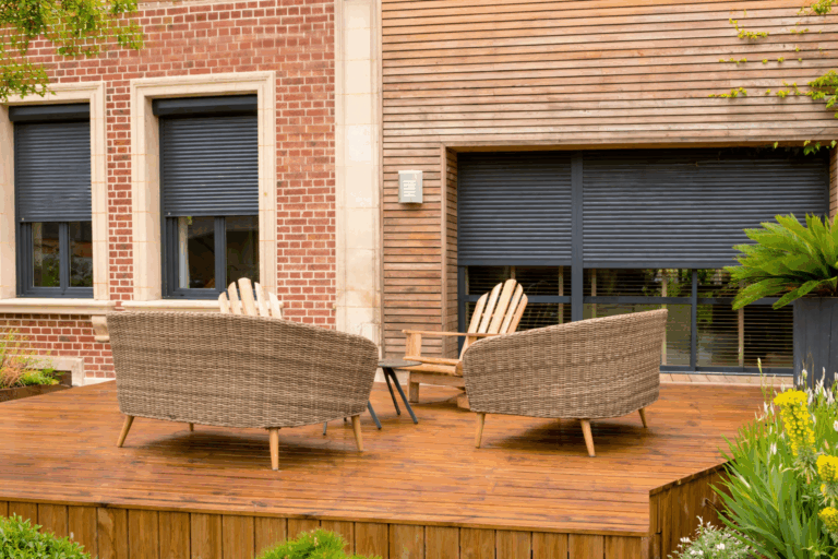 Terrasse en bois avec fauteuils en résine tressée devant des volets roulants anthracite fermés