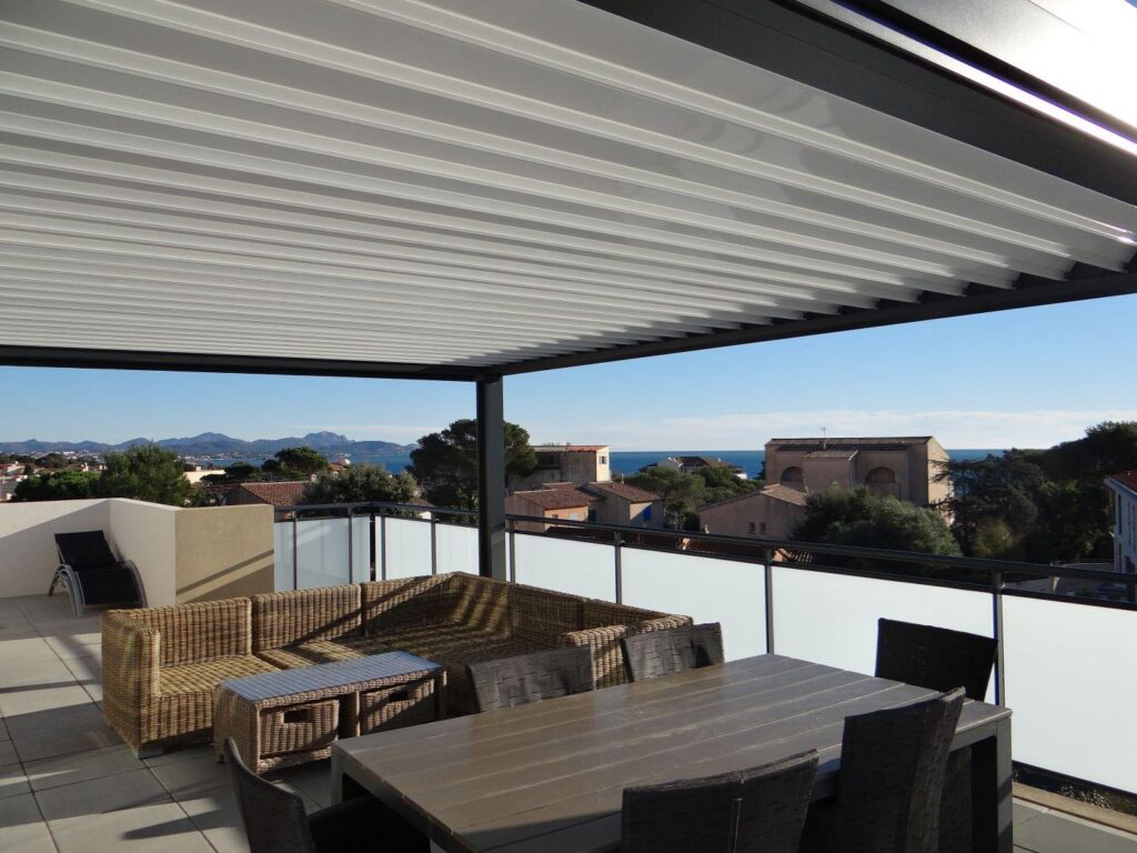 Terrasse en toiture avec pergola bioclimatique, salon en osier et table à manger, vue sur la mer Méditerranée.