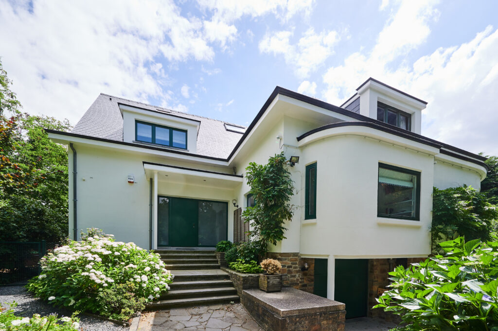 Villa contemporaine blanche avec porte d'entrée et porte de garage vert foncé assorties, toiture en tuiles, jardin avec escalier et hortensias.