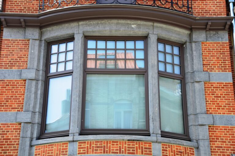 Fenêtres en bois brun à petits carreaux dans une baie vitrée arrondie, façade en briques et pierre ornée.