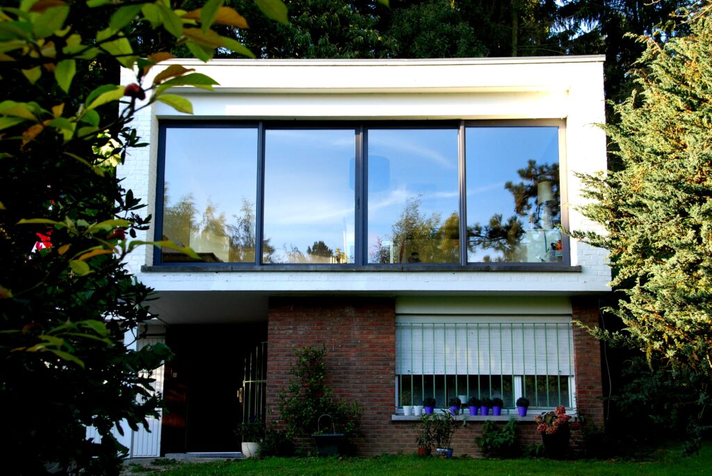 Contemporary white house with large glazed openings, a brick base and roller shutter, tree-lined garden.