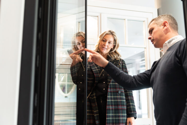 Conseiller Abihome présentant les détails d'un châssis vitré à deux clientes dans un showroom.