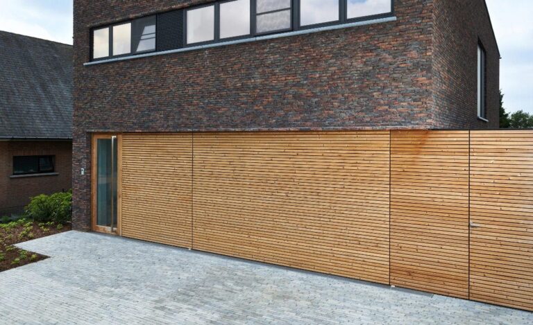 Porte de garage sectionnelle habillée de lattes de bois assortie à la façade, avec porte piétonne vitrée intégrée.